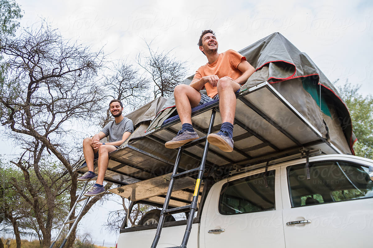Two young happy men sitting on roof tents on top of an off-road vehicle - adventure travel