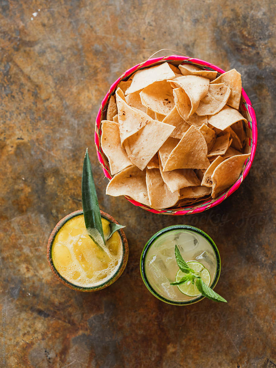 A basket of nachos or tortilla chips with guacamole and a margarita.