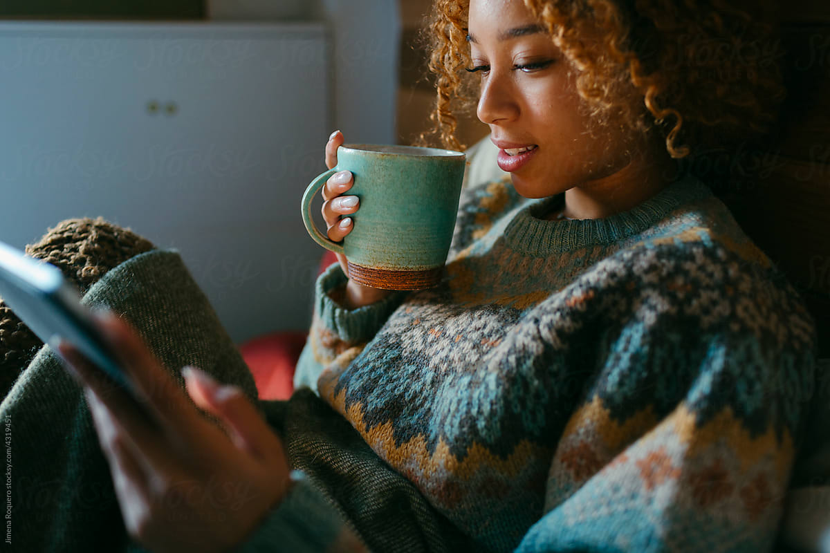 Girl drinks tea in bed and uses tablet in hygge season