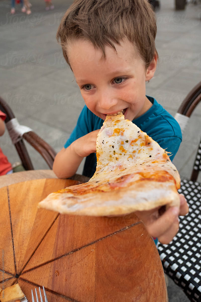 Happy kid eating a pizza slice outdoors