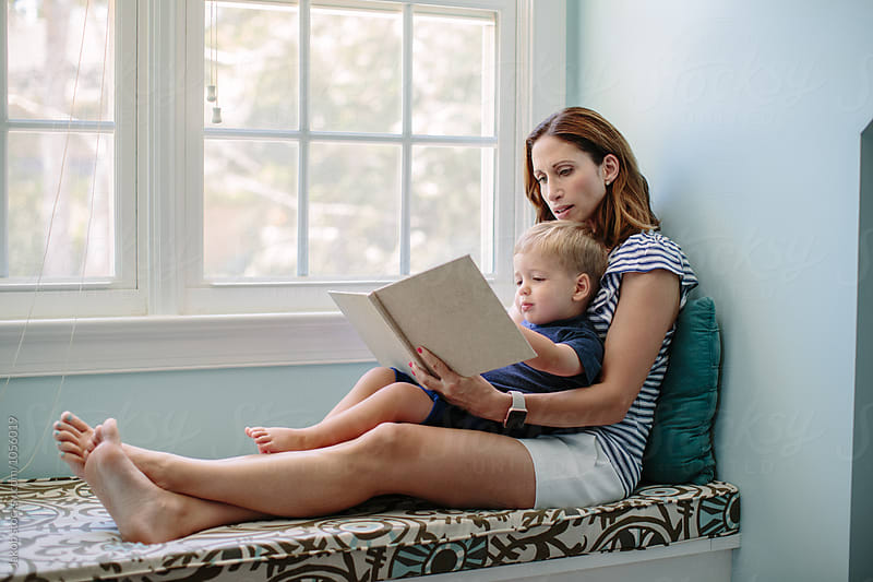 Mother sitting on a window sill reading a book to her son