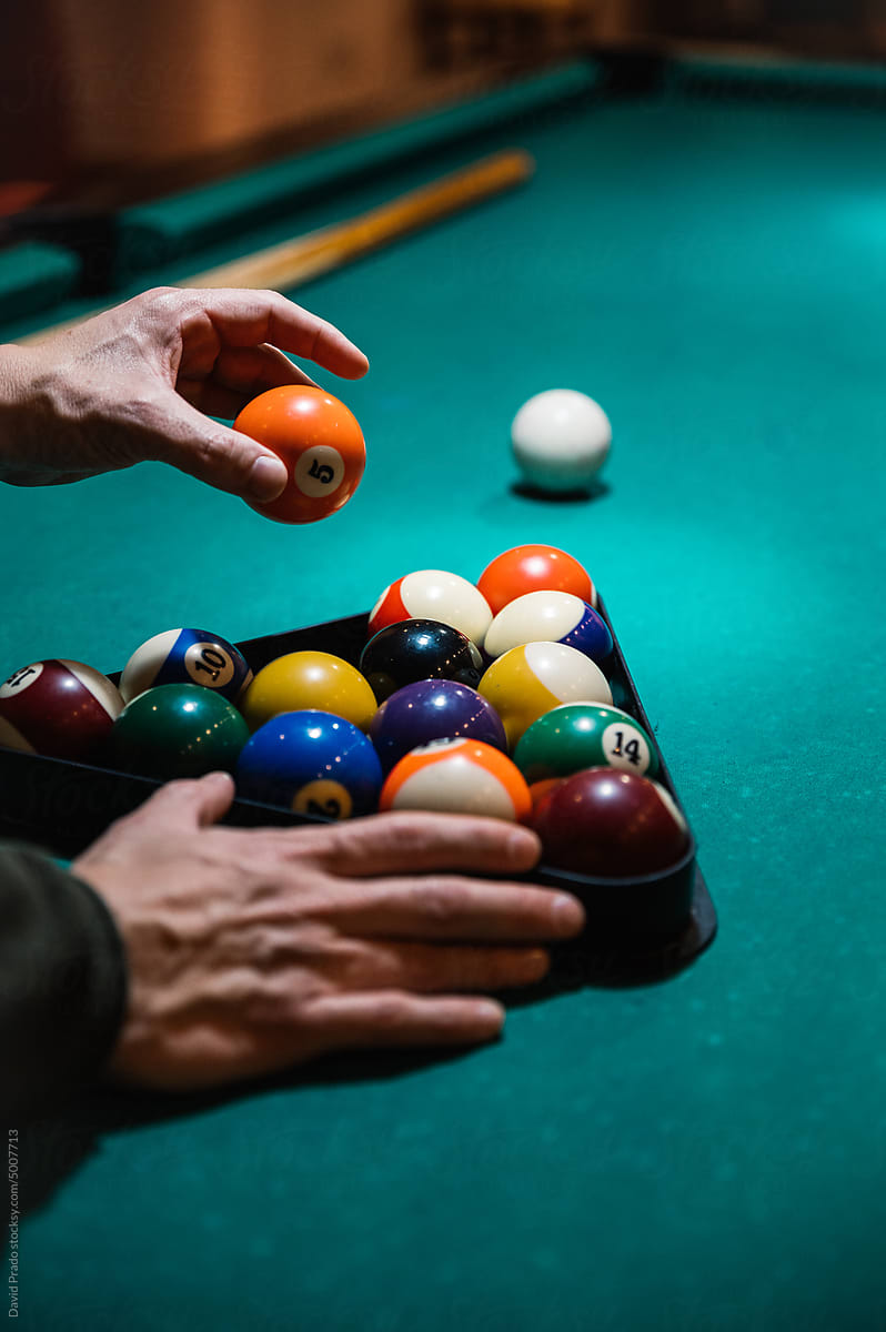 Crop man arranging balls in rack on billiard table