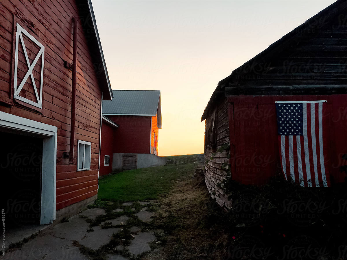 American flag on a red barn at a farm in summer at sunset