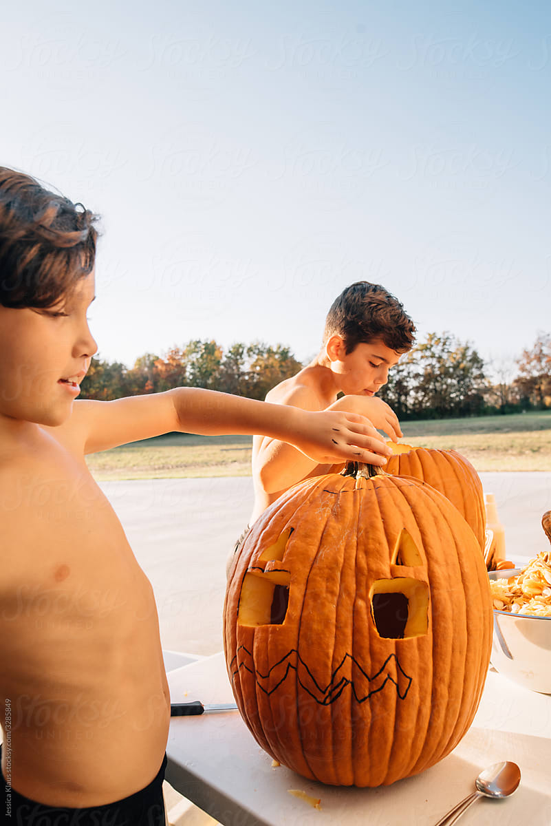 Boys carving pumpkins together.