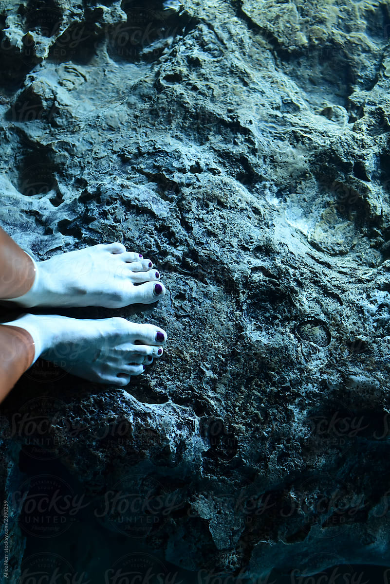 Feet in glowing blue water on rock