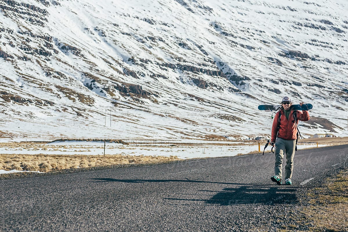 Skier walking alone carrying skis long an empty road in Iceland