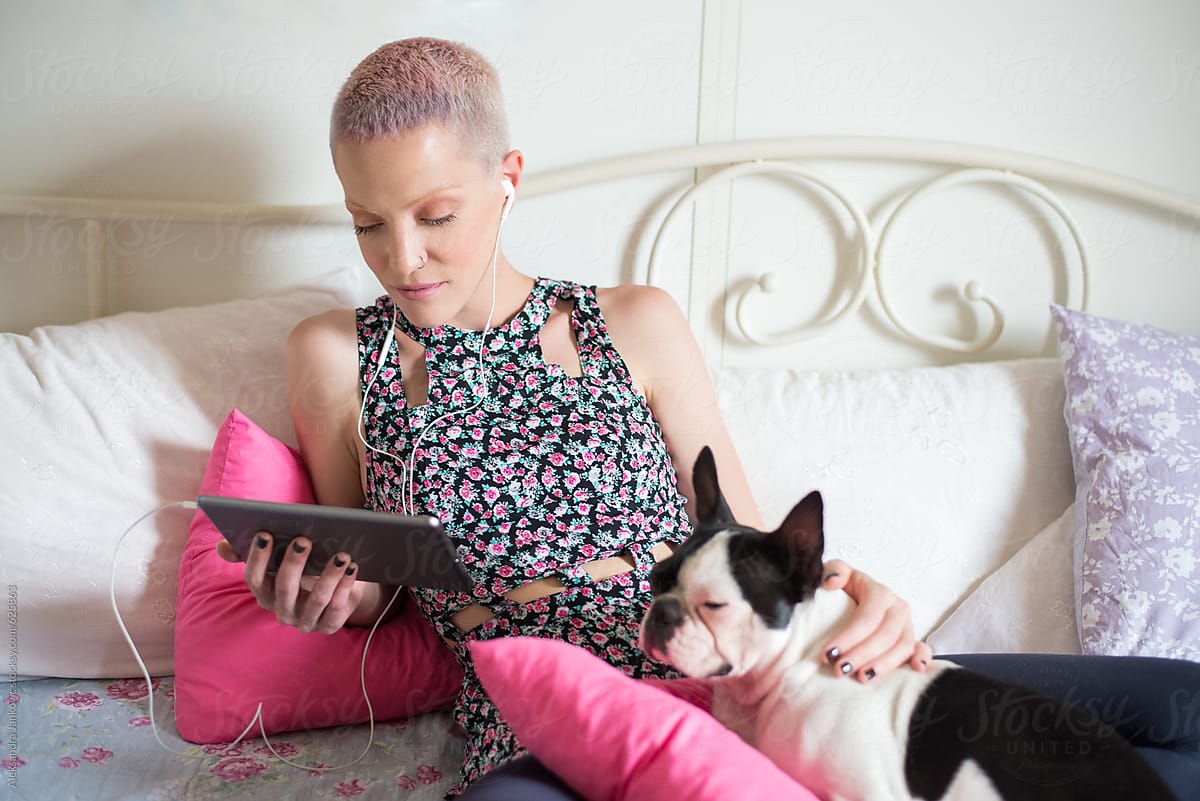 Stylish Young Woman Sitting On The Bed With Her Dog And Using Tablet Computer