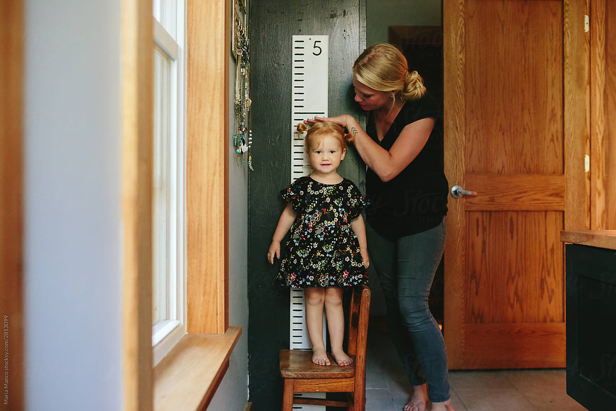 mother measures daughters height on wall growth chart