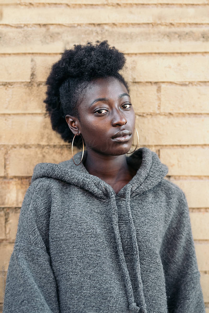 Serious black woman in sweatshirt near brick wall