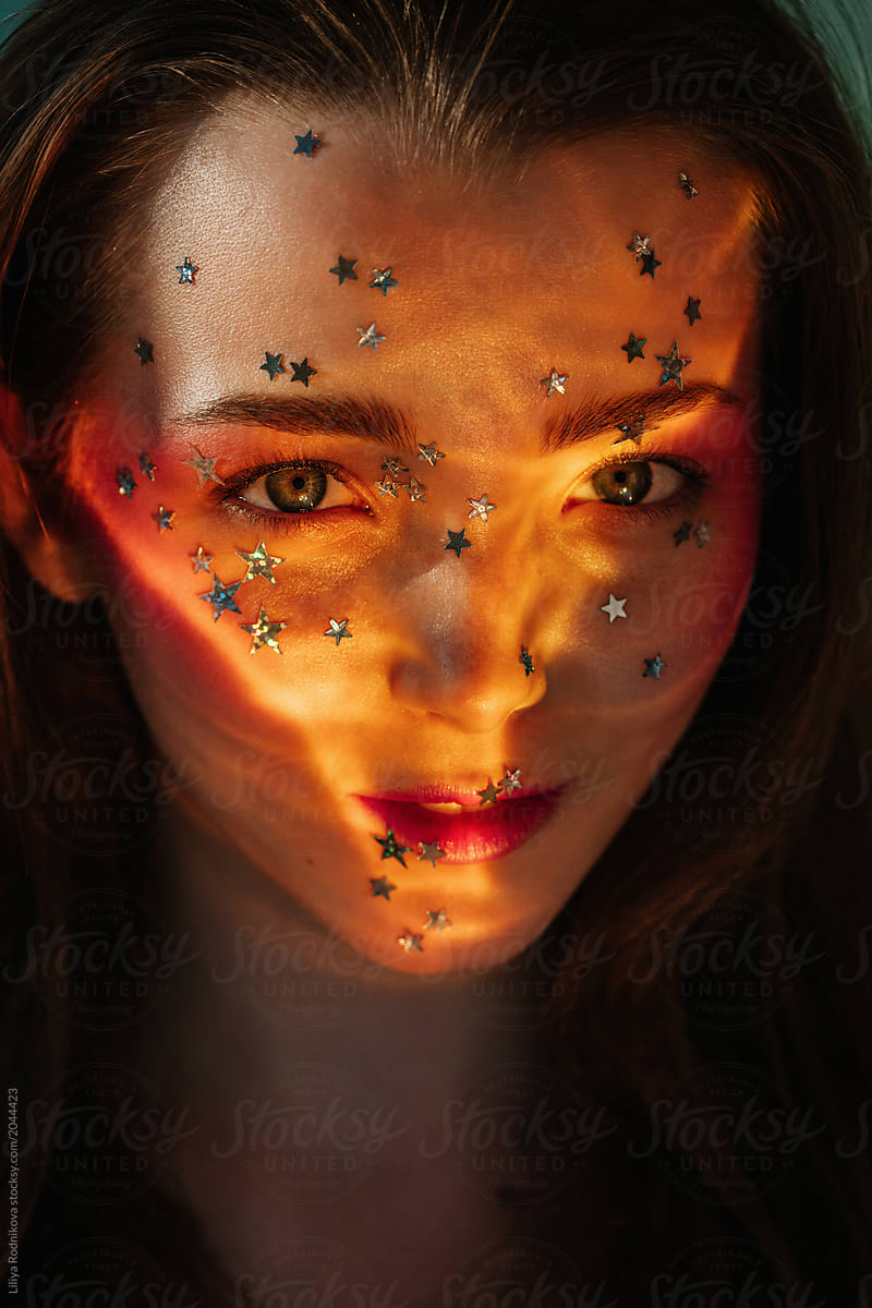 Headshot portrait of amazing girl with silver stars on her face in bright yellow background