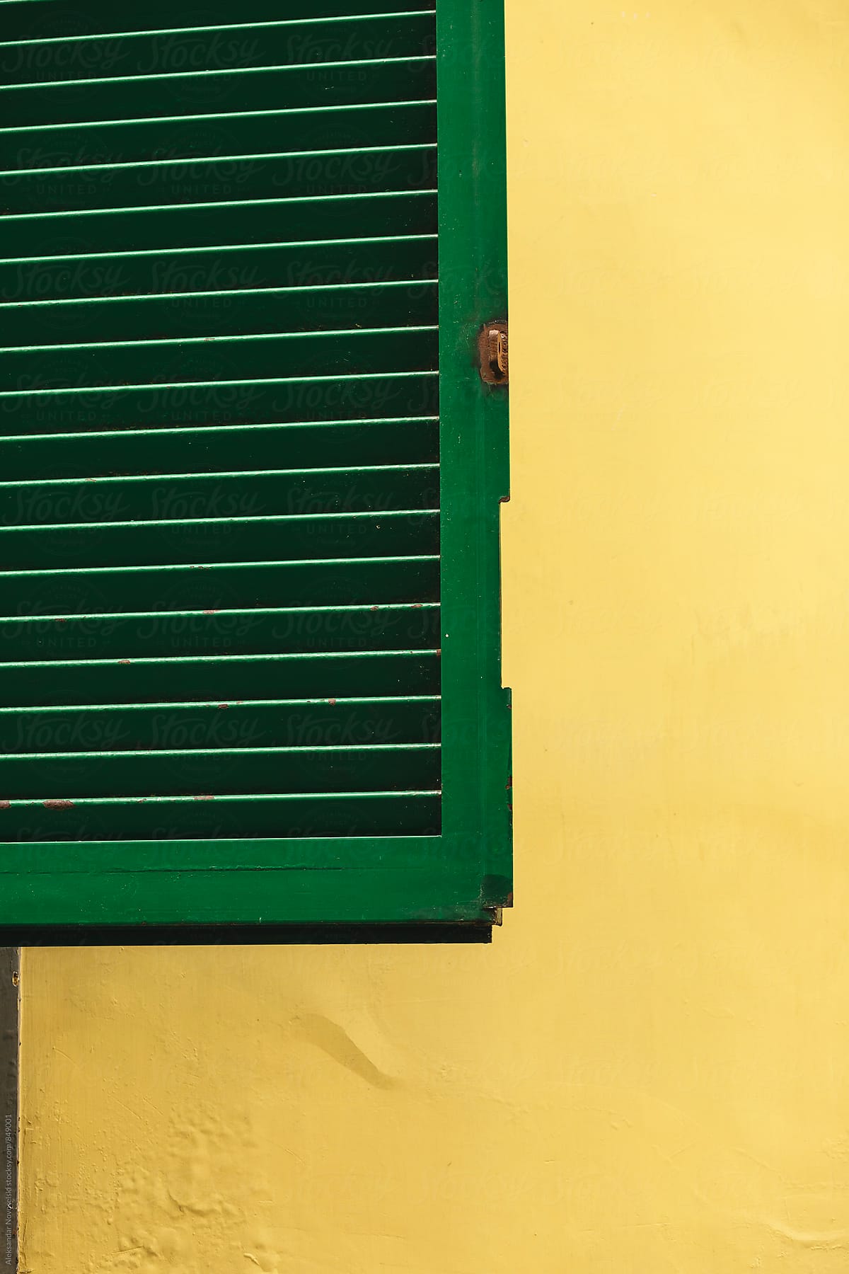 Green window cover against yellow wall