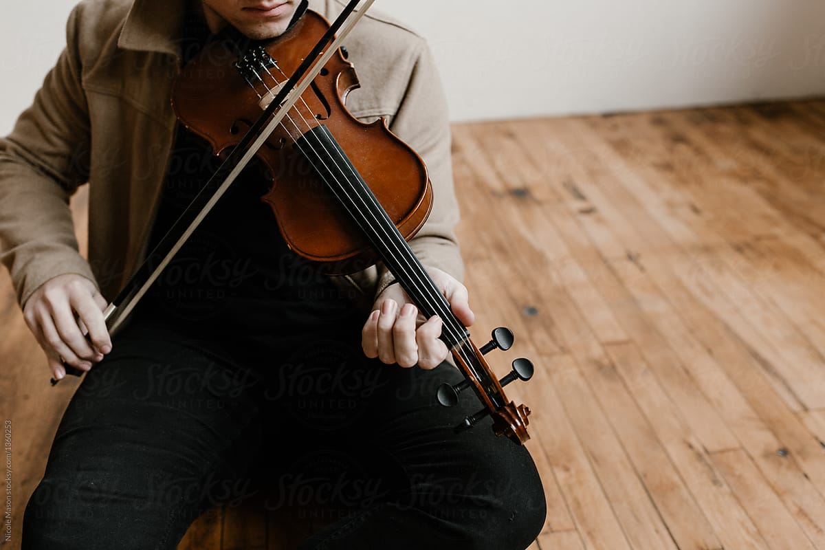 young stylish man sitting on studio floor playing violin