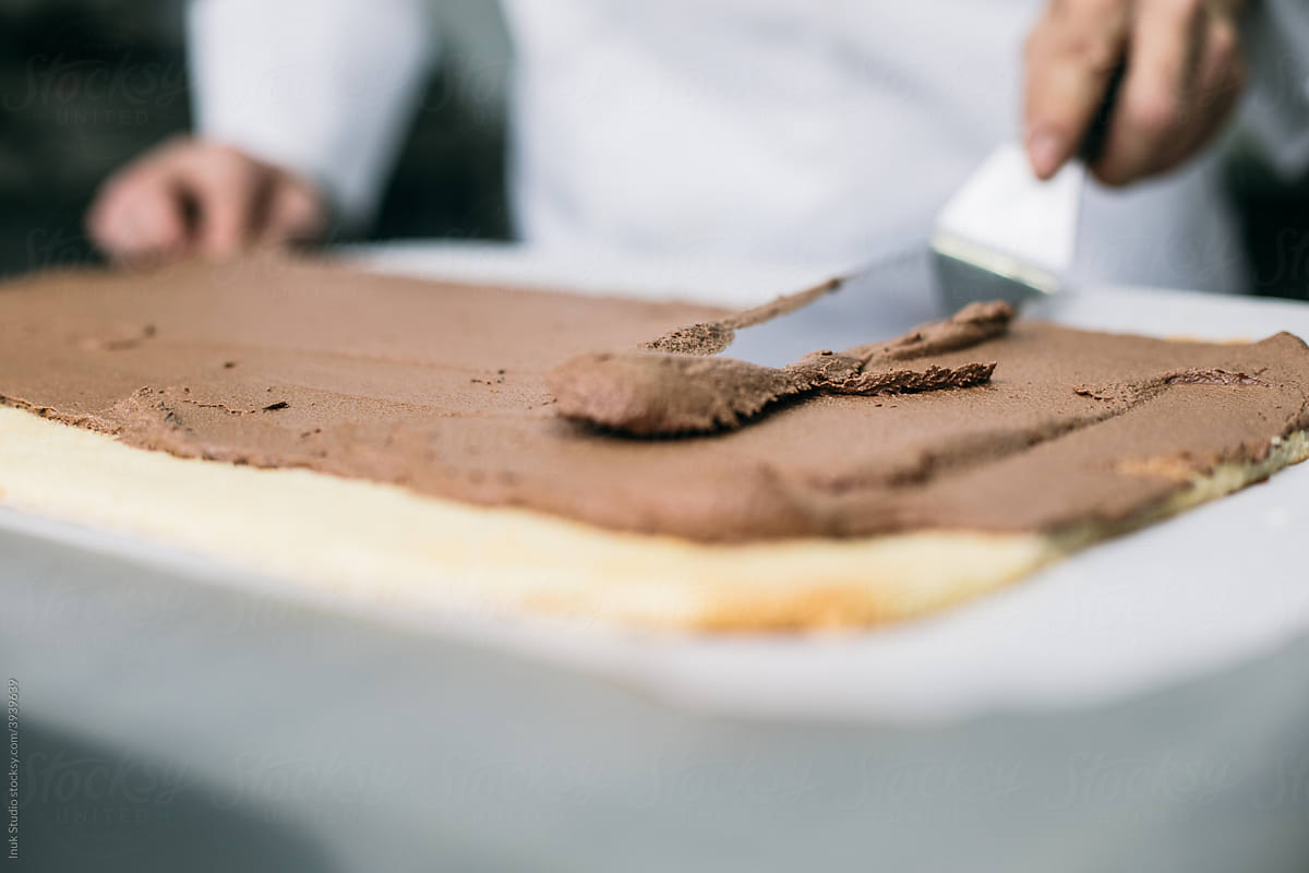 Chef spreading chocolate cream on biscuit layer