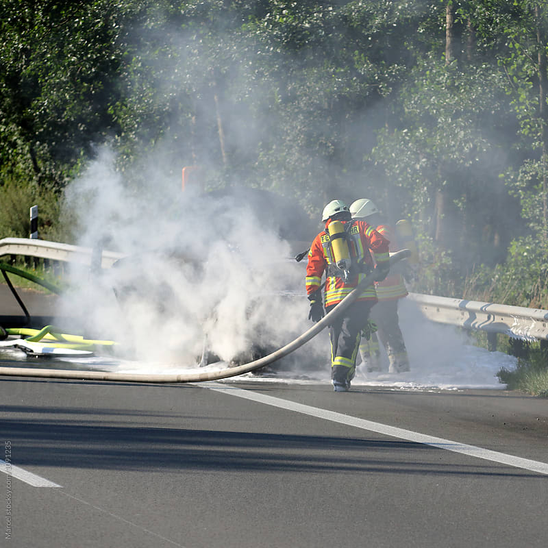 Firefighters extinguishing a burning car on the highway