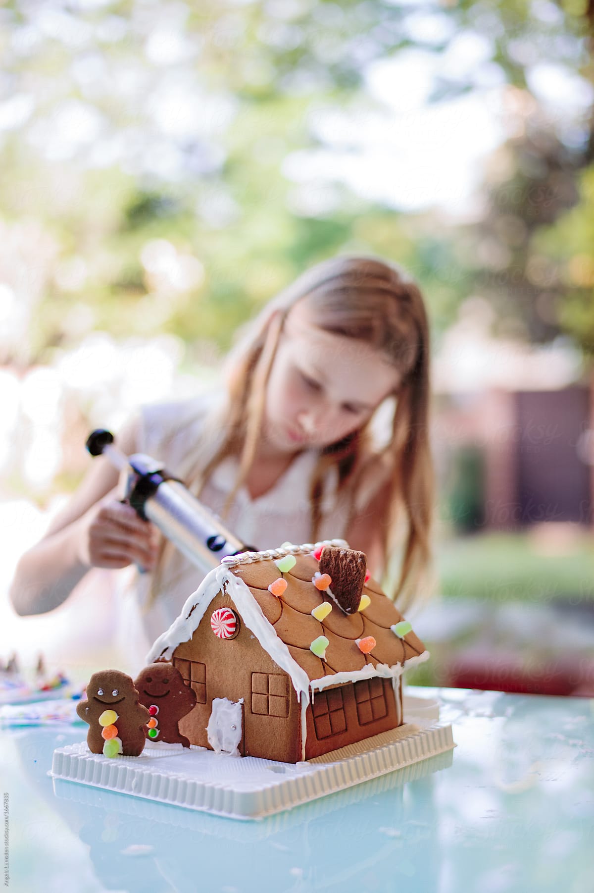 Girl Icing A Gingerbread House At Christmas By Angela Lumsden Stocksy