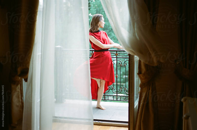 A film portrait of young beautiful woman with red dress standing on the balcony