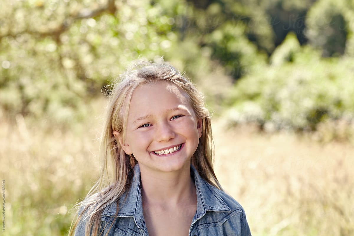 Portrait Of Little Girl With Blonde Hair Outdoors Smiling By
