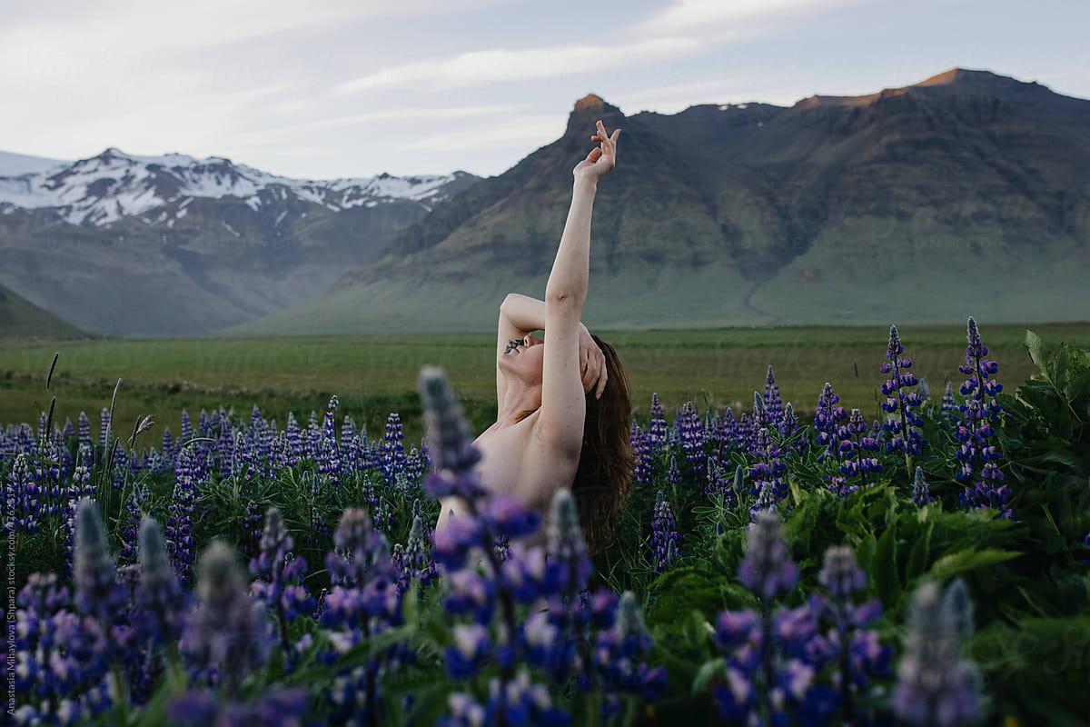 Naked woman standing in purple flower field looking at the mountains