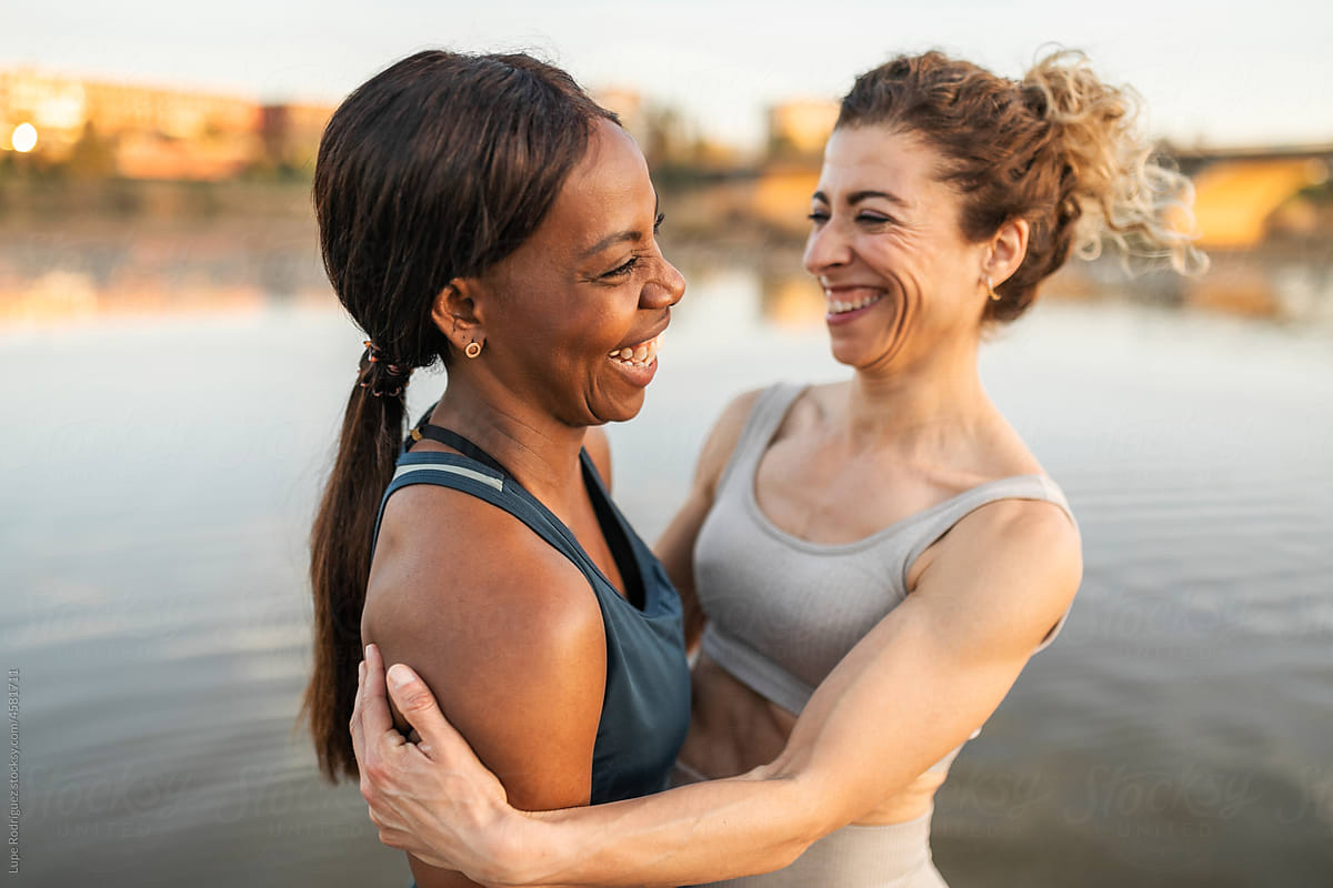 Middle-aged multiracial female friends embrace on a river jetty