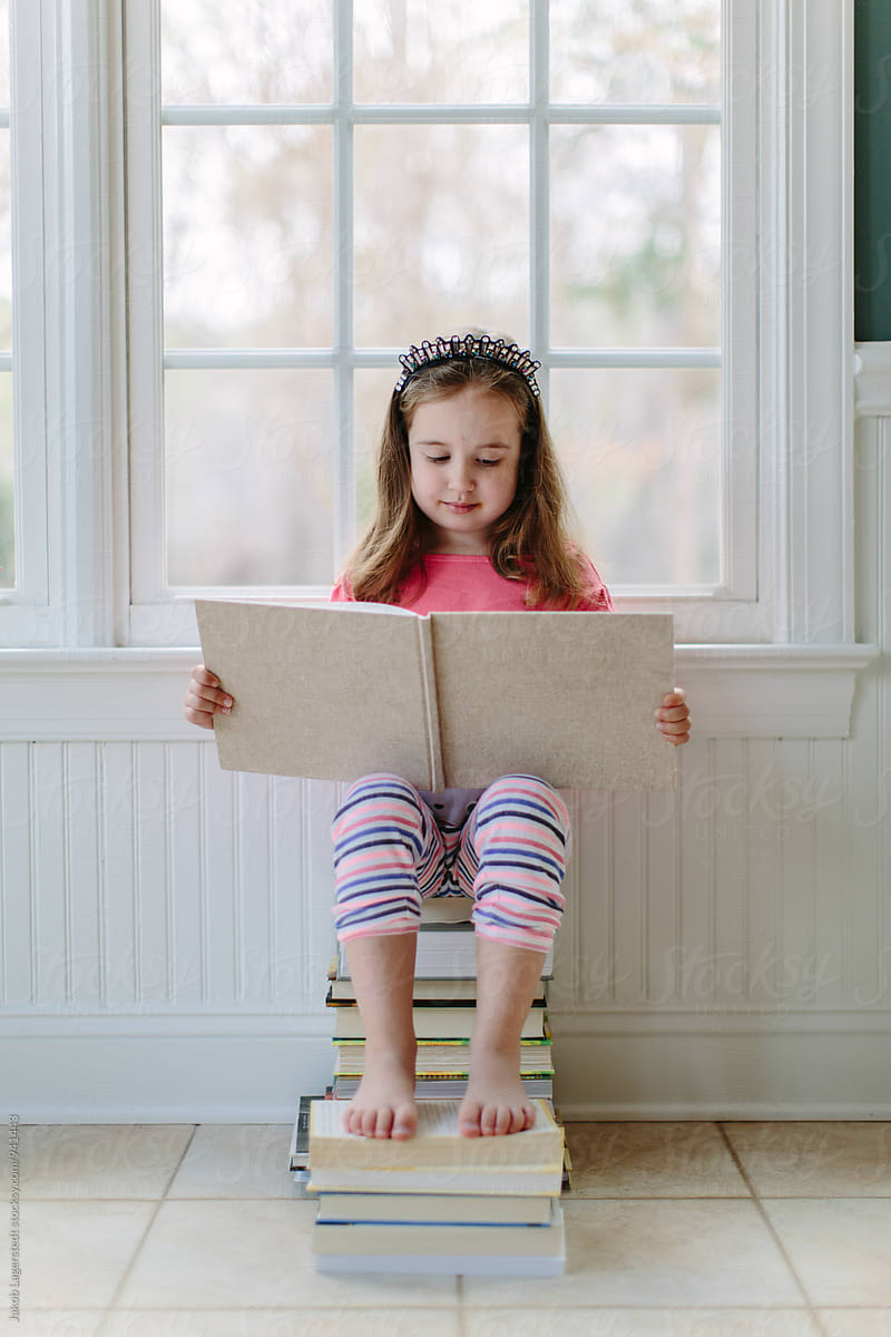 Cute young girl sitting on a stack of books reading