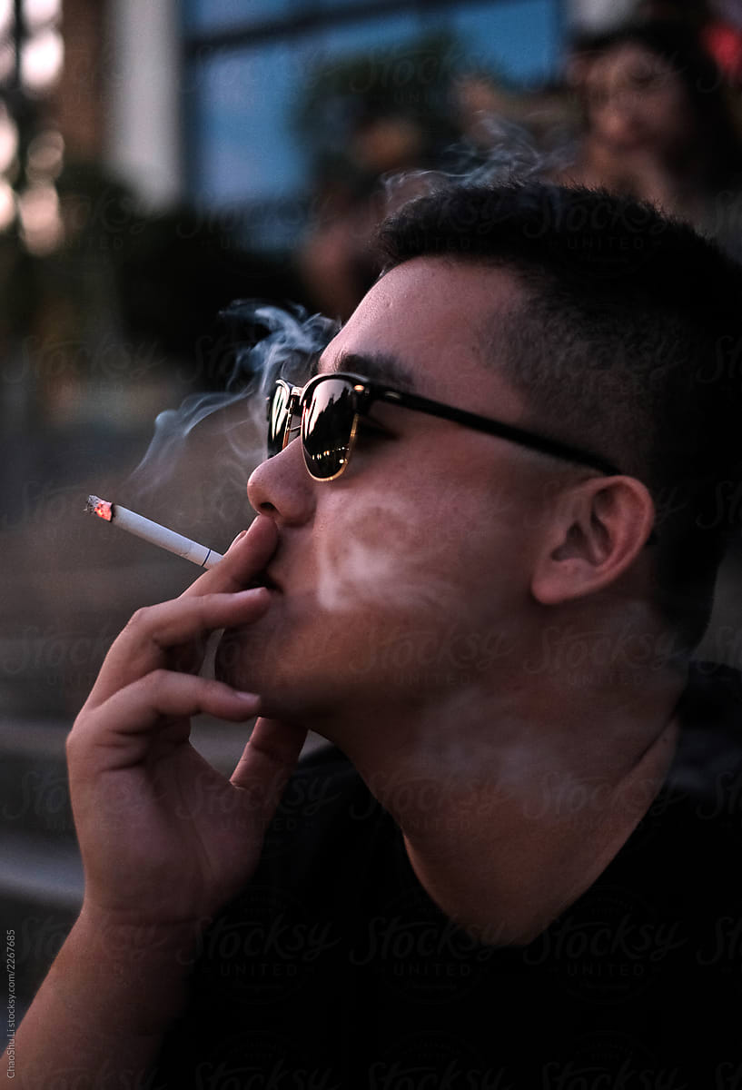 Asian young man wearing sunglasses smoking a cigarette at the music festival scene