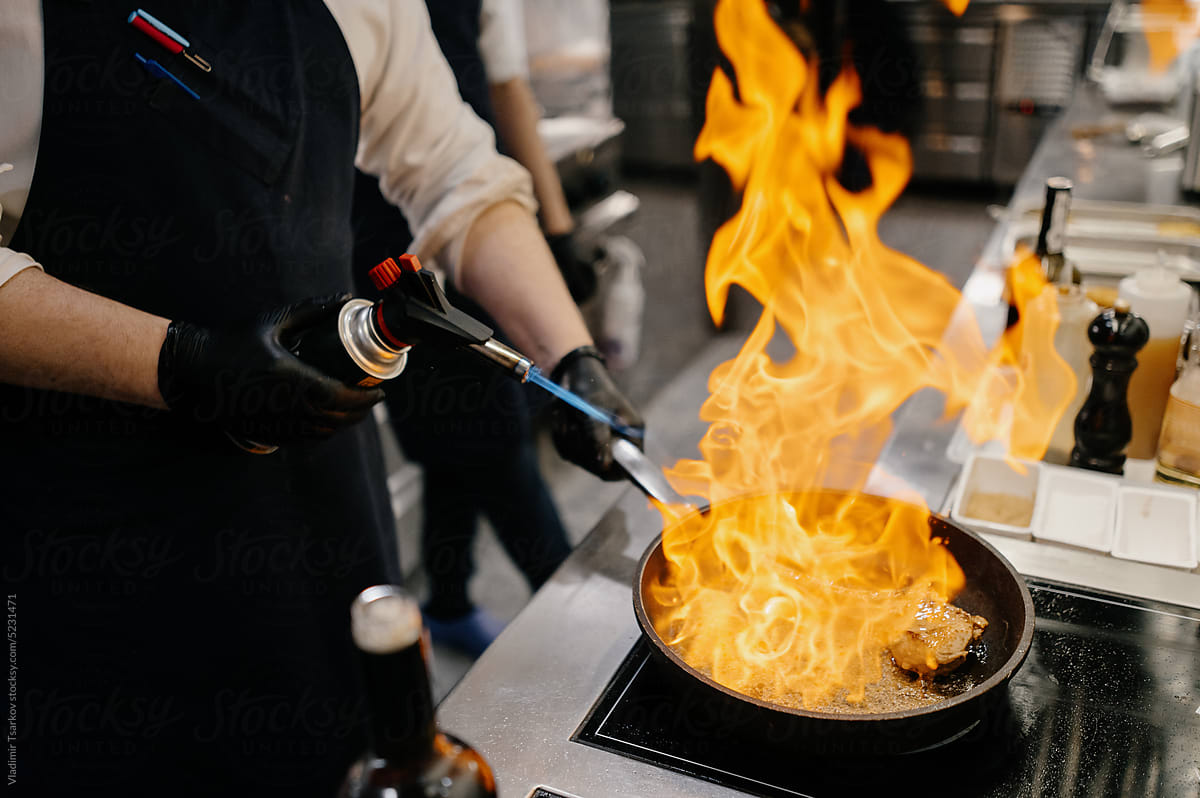 Chef using torch while preparing meat in burning pan