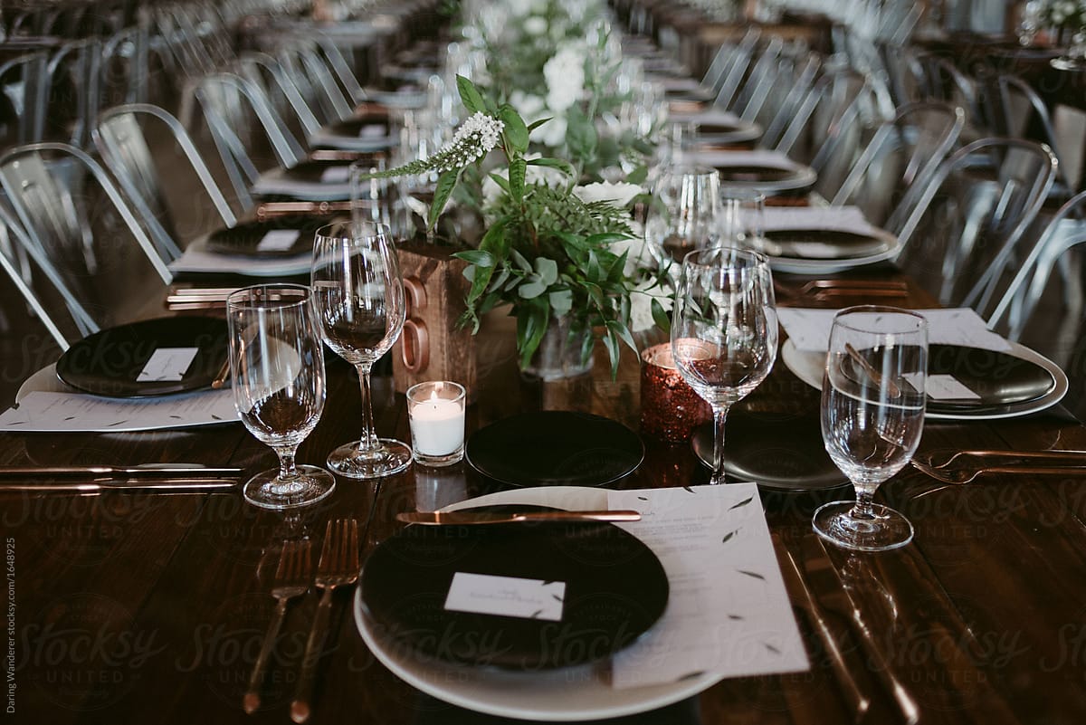 Long harvest tables with simple greenery and copper details in industrial setting for wedding