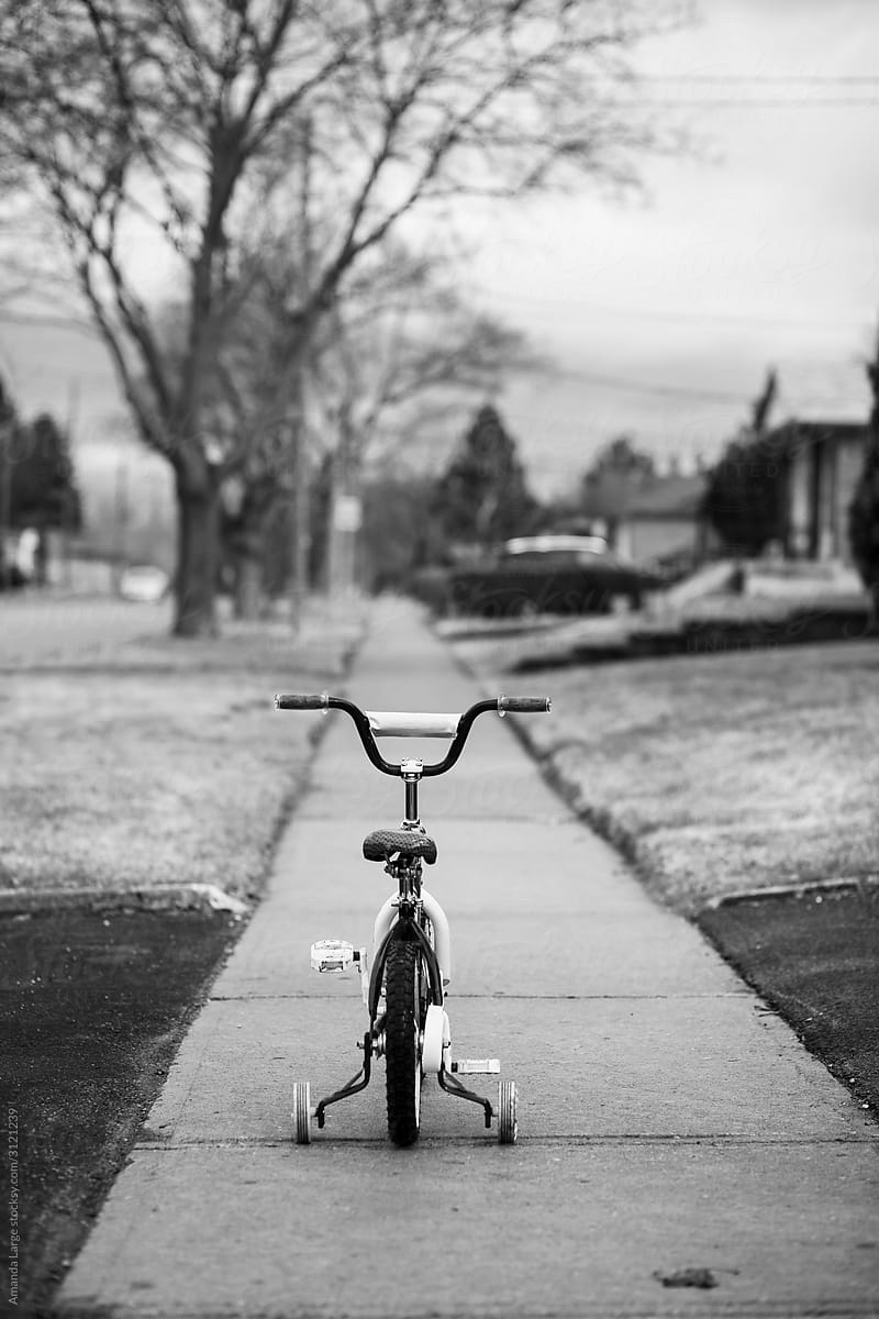 A bike with training wheels sits in the middle of a sidewalk.