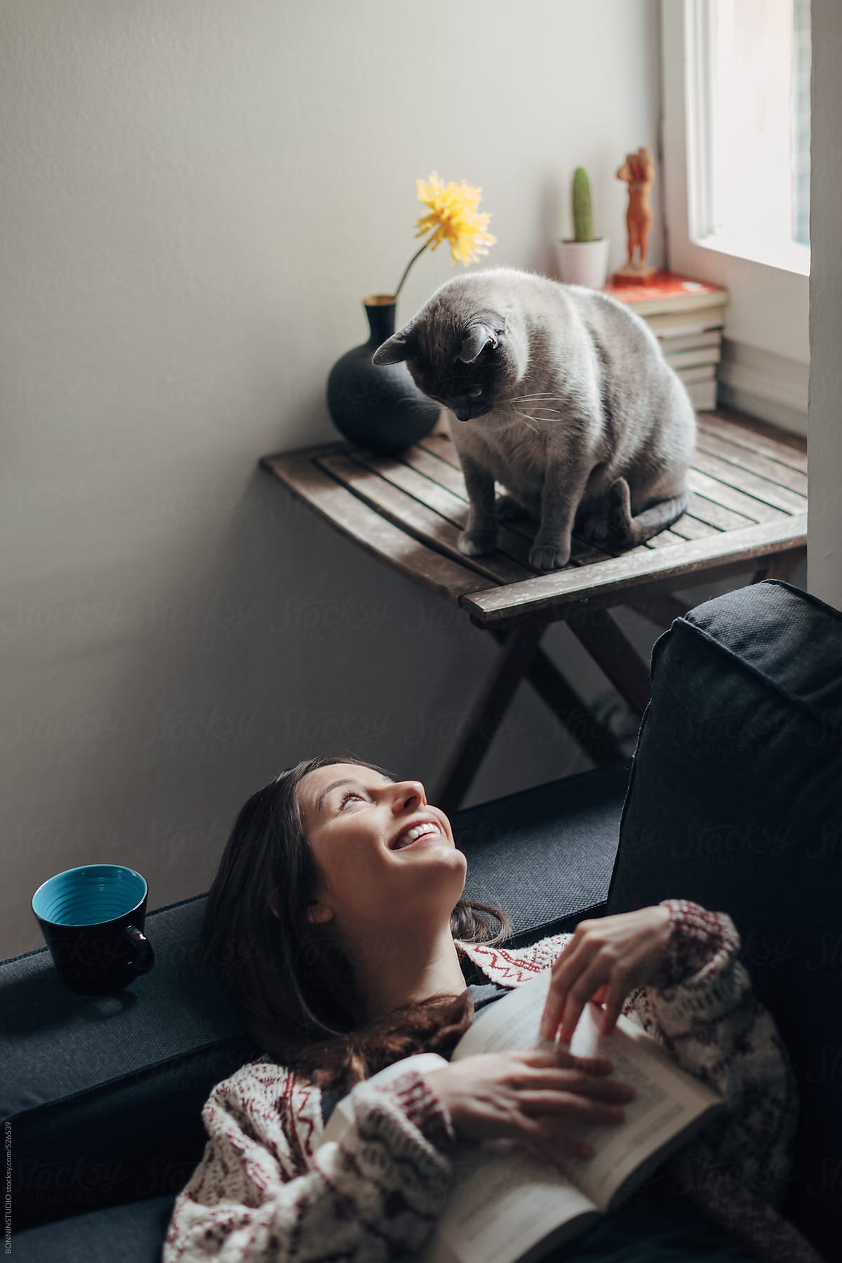 Woman with a book and her cute cat at home.