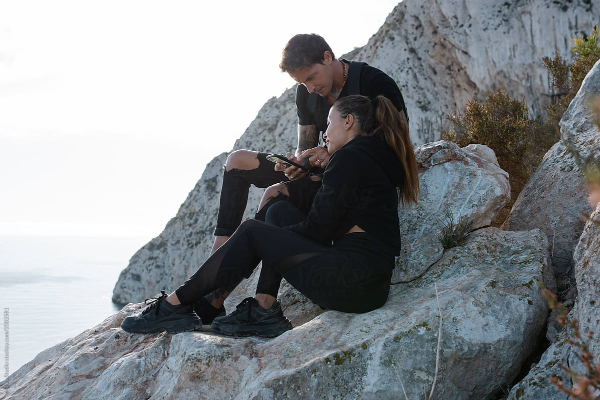 Couple using smartphone on rocky seashore