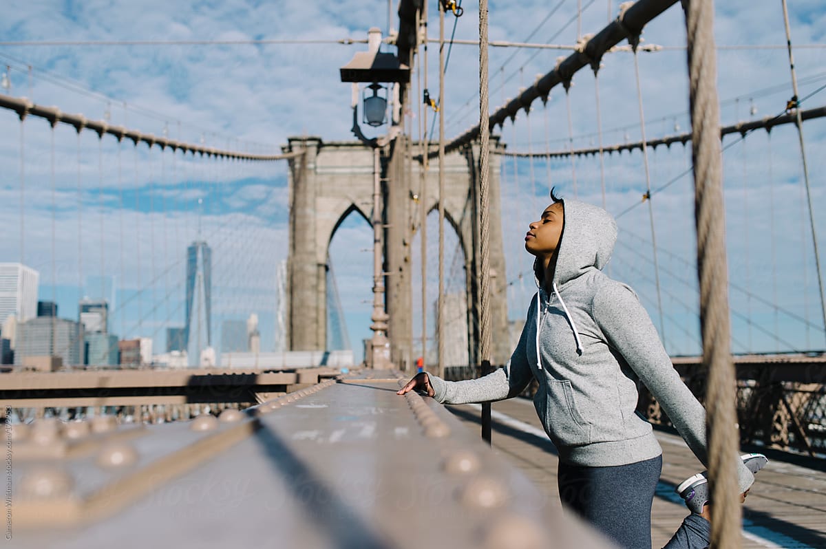 Young woman stretching during a run across the Brooklyn Bridge