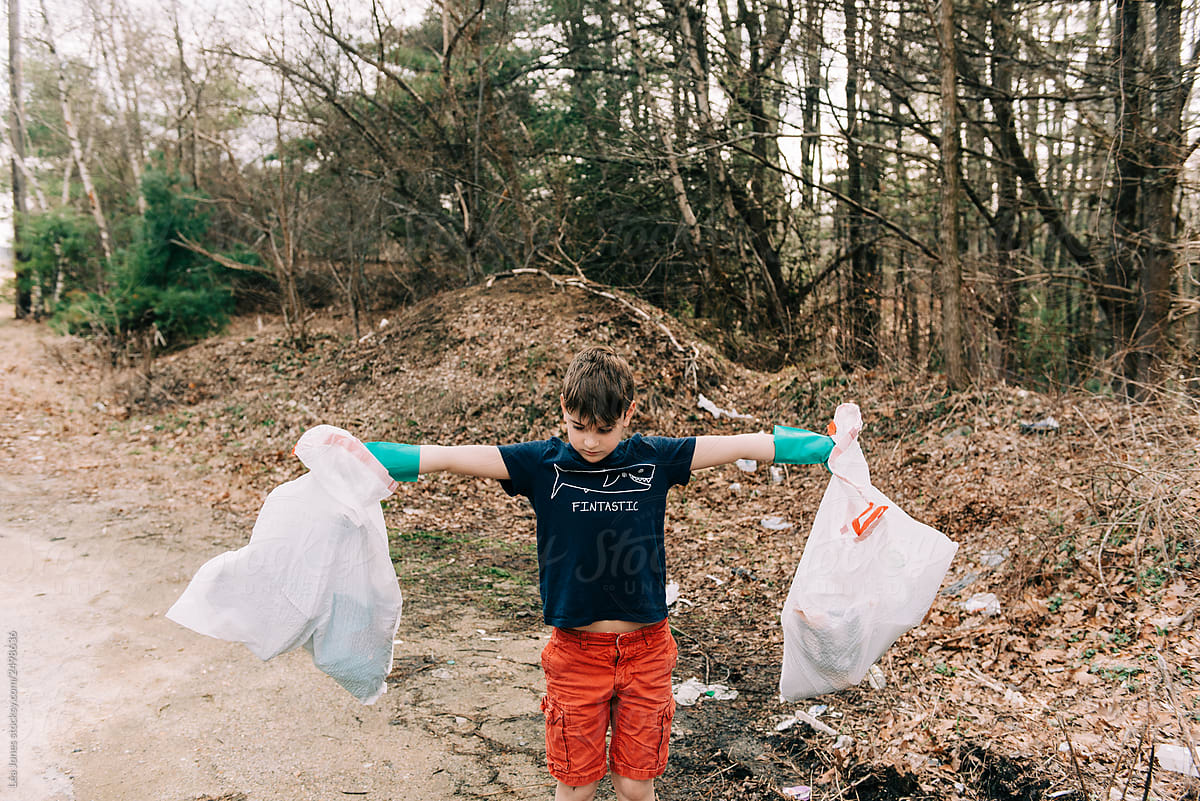 stock photo of little boy posing with trash bags that he picked up on earth day
