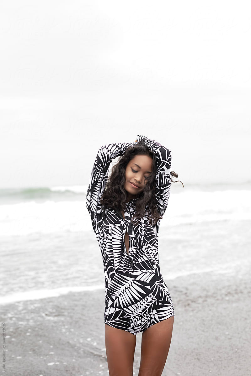A dark asian woman with long curly hair is wearing a fashionable black and white rash guard.