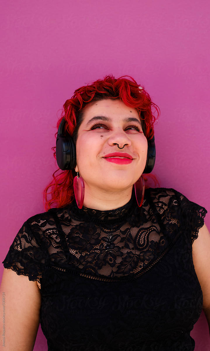 Happy queer person with headphones over pink background