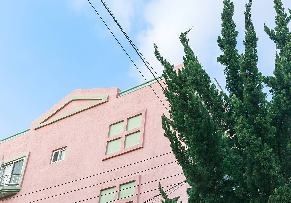 Pink building and sunny sky seen behind trees.