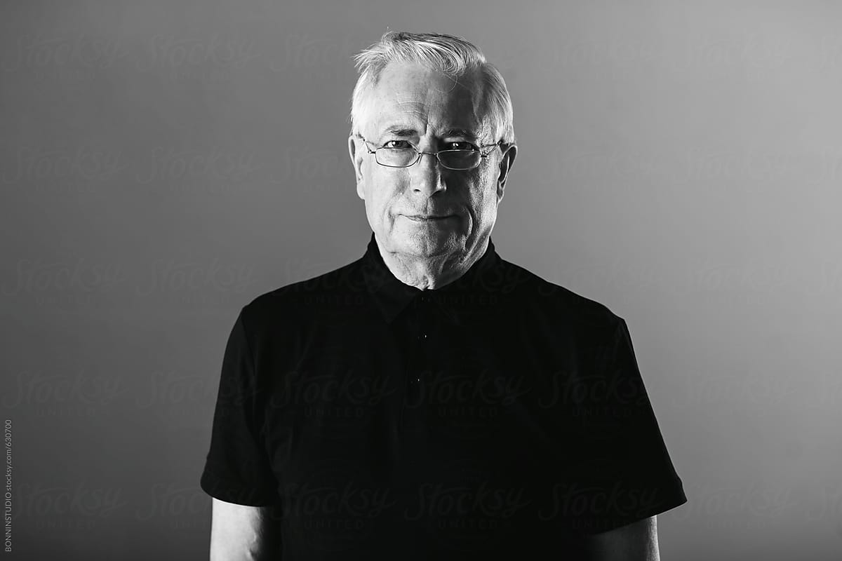 Portrait of an elderly man standing indoors. Black and white photo.