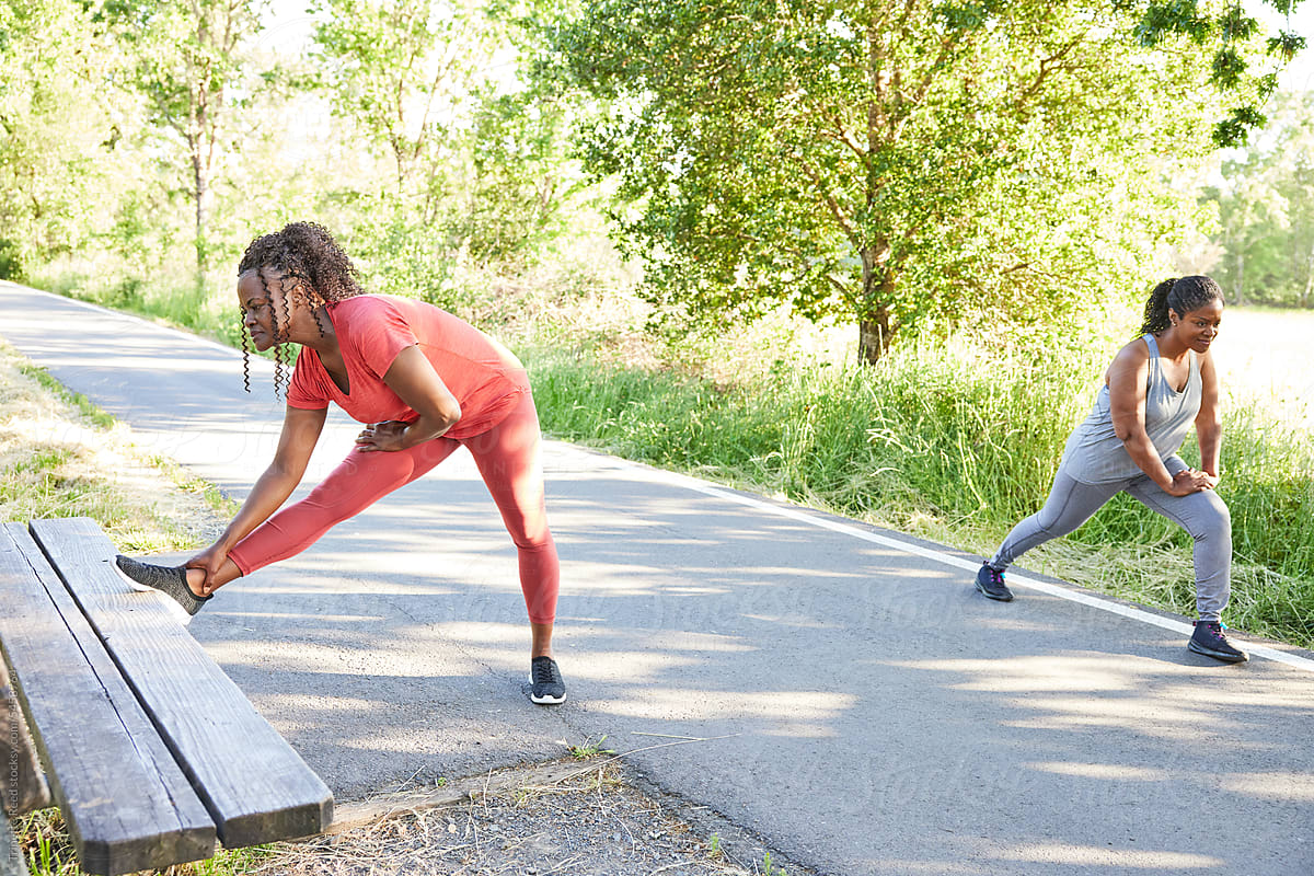 Mature Black women friends stretching together in nature before a run