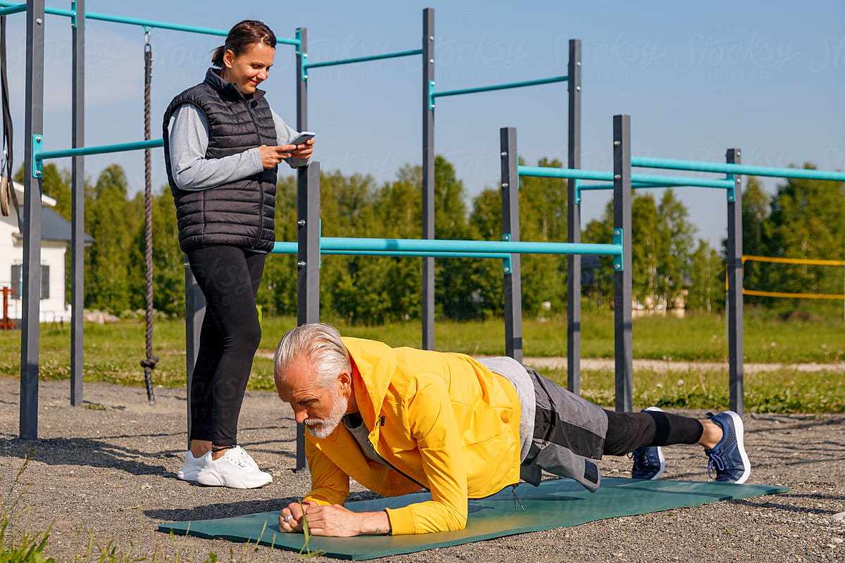 Middle aged man doing plank exercise near woman with timer