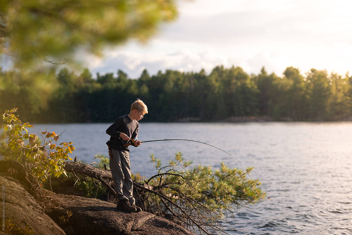 Boy on fishing trip vacation alongside lake gets bite on line