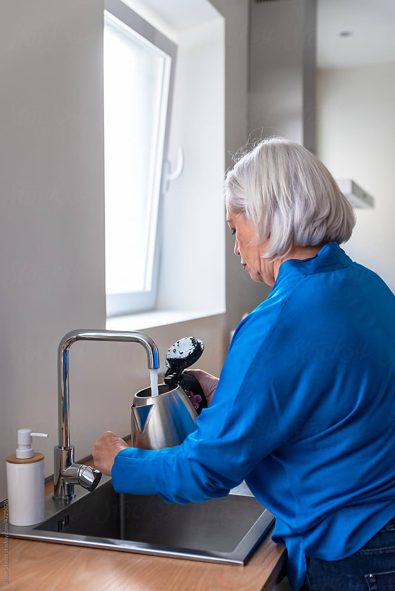 Mature woman pouring water into kettle