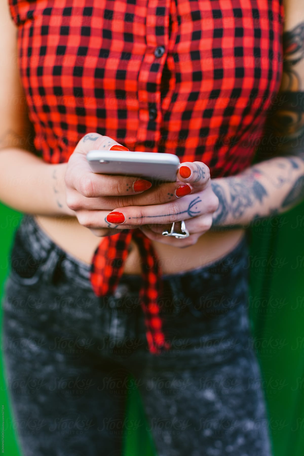 Closeup of a young alternative woman using her smartphone in front a green wall.