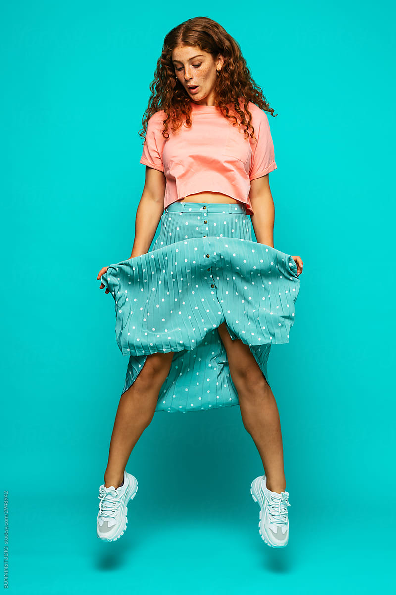 Fashionable young woman holding hem of skirt and jumping up