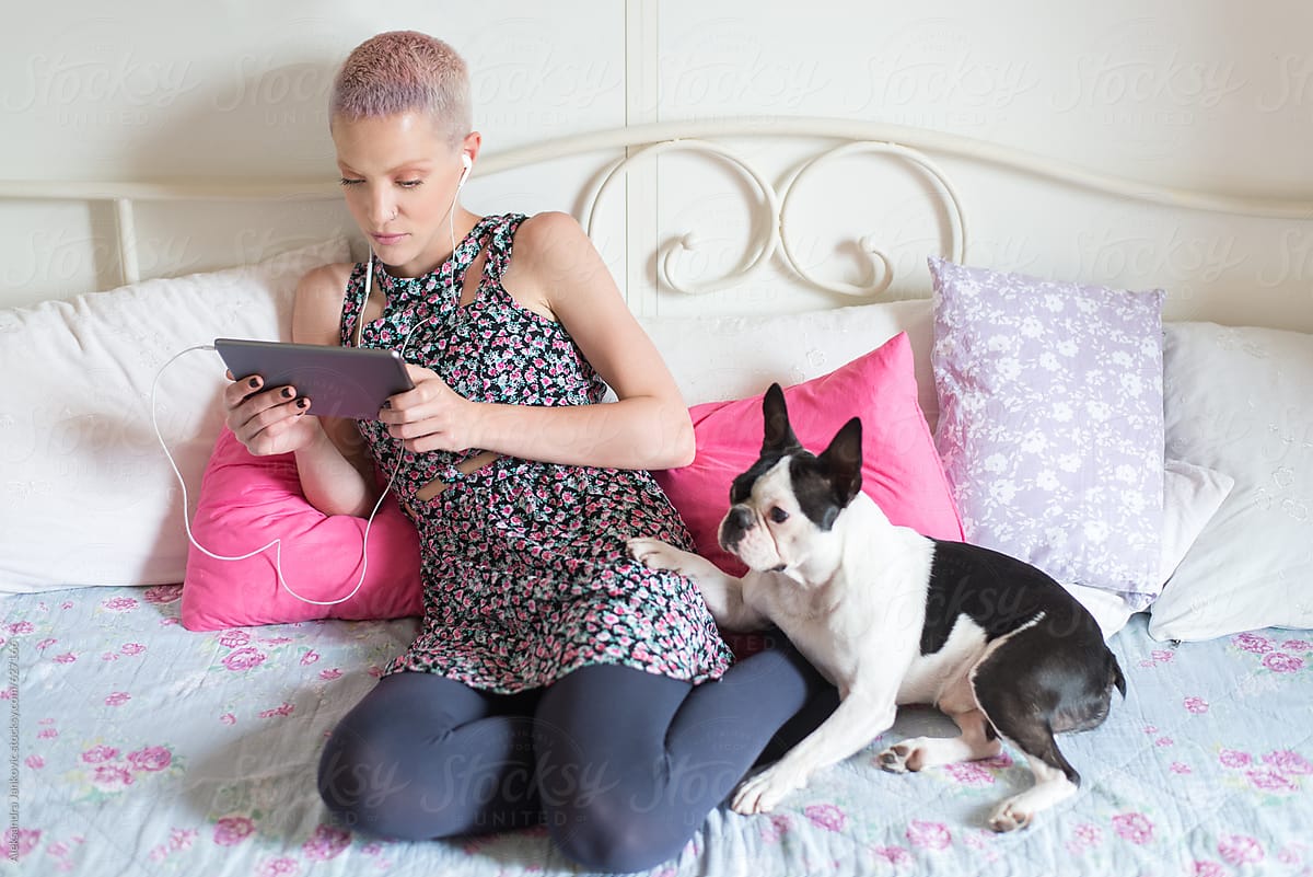 Stylish Young Woman Sitting On The Bed With Her Dog And Using Tablet Computer