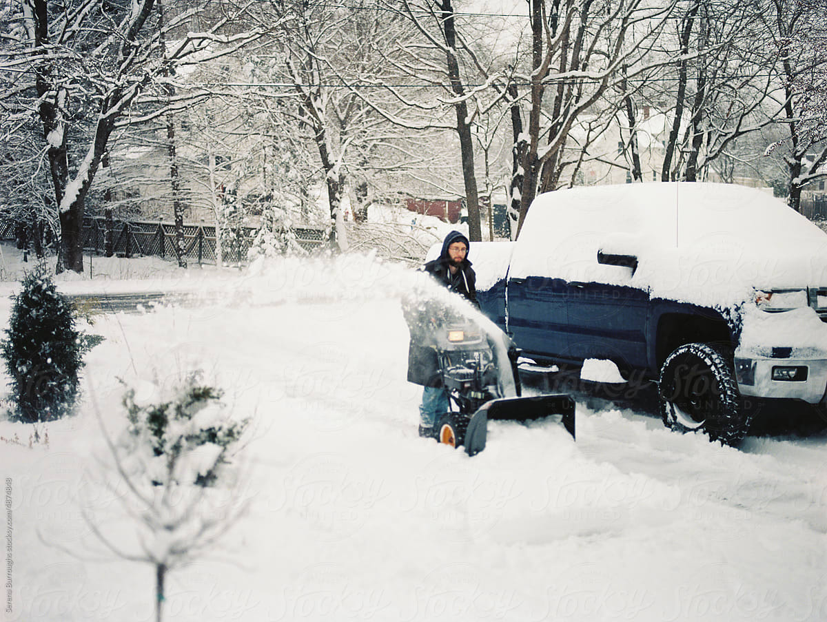 man clearing heavy snow in winter in his driveway with a snowblower