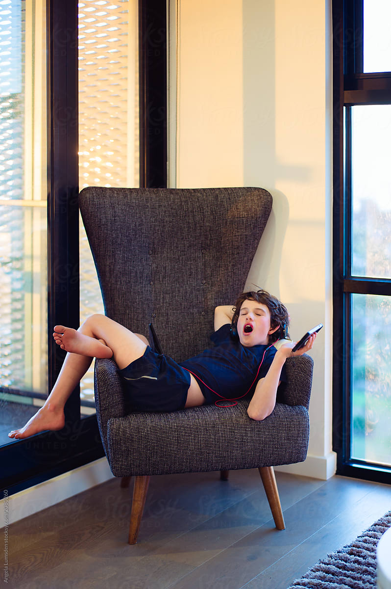 Boy yawning on a chair with headphones, a tablet and a phone