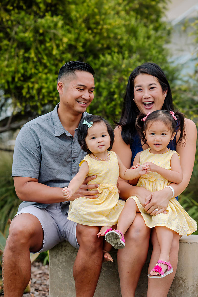 Happy asian family with two daughters sitting on concrete ledge outdoors