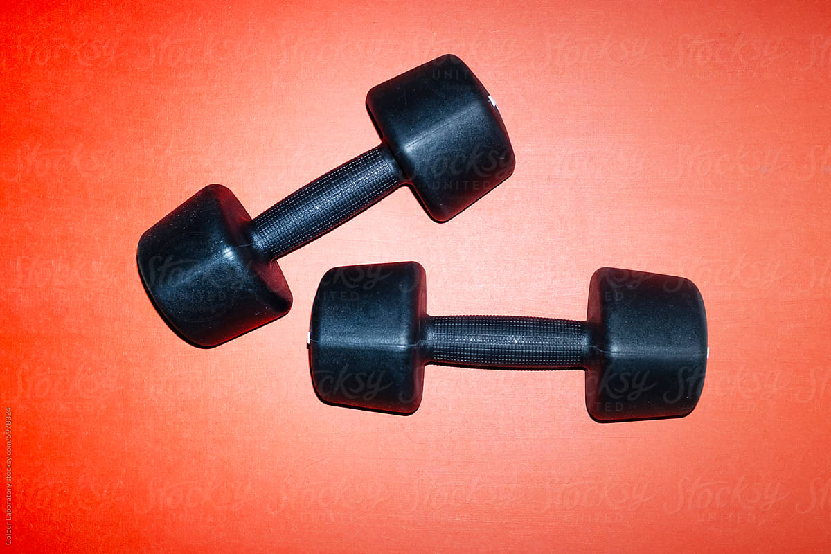 Matte black metal dumbbells on red surface with hard direct flashlight