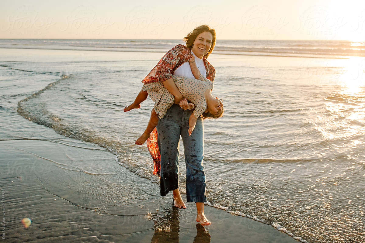 Mom carrying girl on beach at sunset