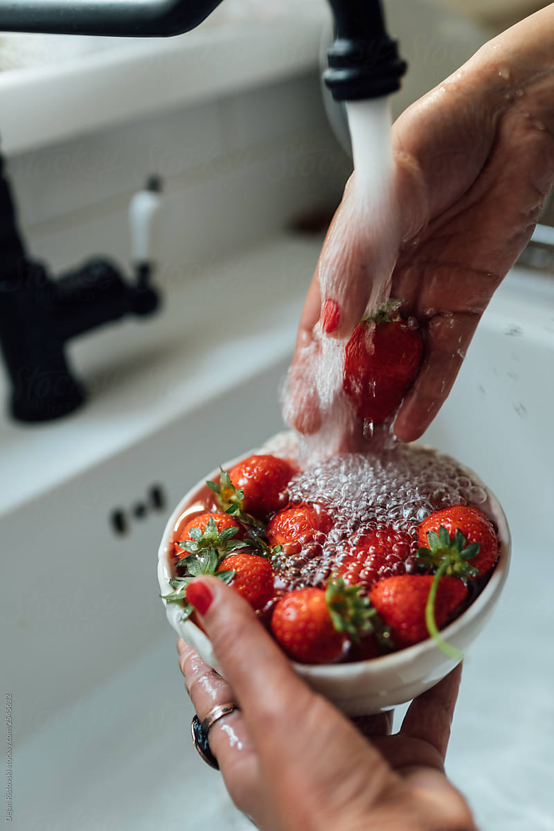 Woman washing strawberries under a running water