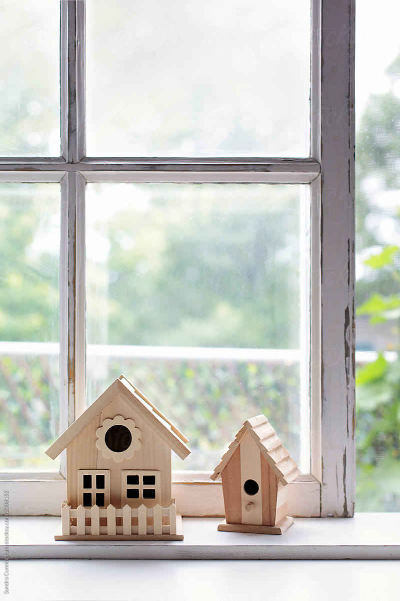 Two wooden bird houses on sunny window sill